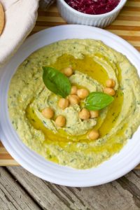 Greenish yellow Lemon Mint Basil Hummus Dip on a white plate, with chickpeas and basil leaves for garnish