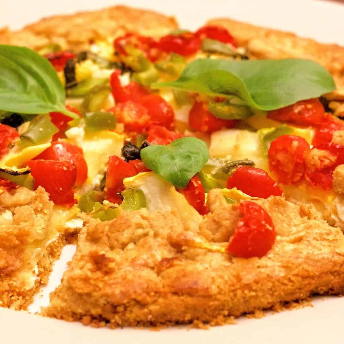 Whole wheat herbed patty pan squash tomato tart, sliced into wedged, with bright red cherry tomatoes and green basil leaves on top
