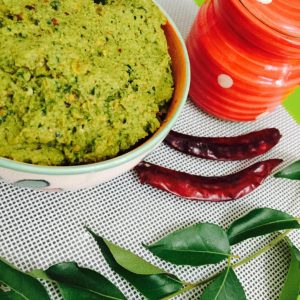 A bowl of peerkangai thogaiyal or ridge gourd dal chutney, with a red jar, red chilies and green curry leaves alongside 