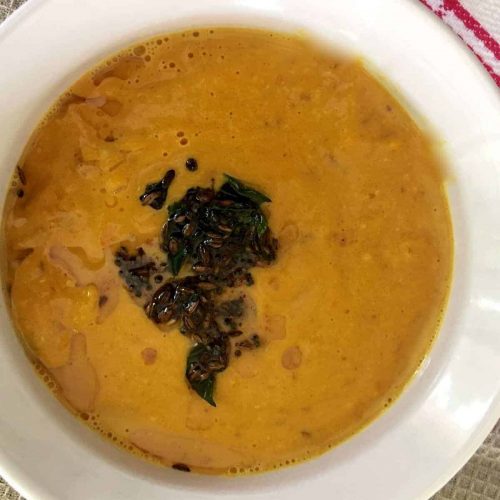 A white bowl with mustard orange coloured chutney tempered with cumin and chili, tomato peanut orange peel chutney Andhra Style