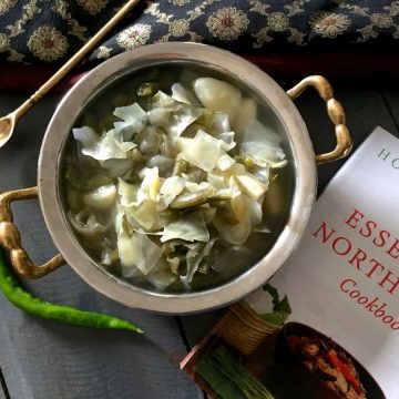 Oying Vegetable Stew from Arunachal Pradesh in NE India. Brass bowl with stew of cabbage, potato and beans with Cookbook and a green chilli by the side