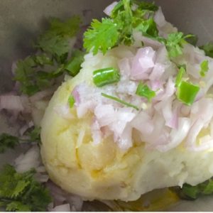 A heap of mashed potatoes with onions, cilantro and green chilli and with mustard oil dripping yellow at one side