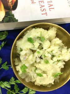 Alu Pitika - mashed potatoes in a bowl with cilantro garnish and a book just visible at the edge