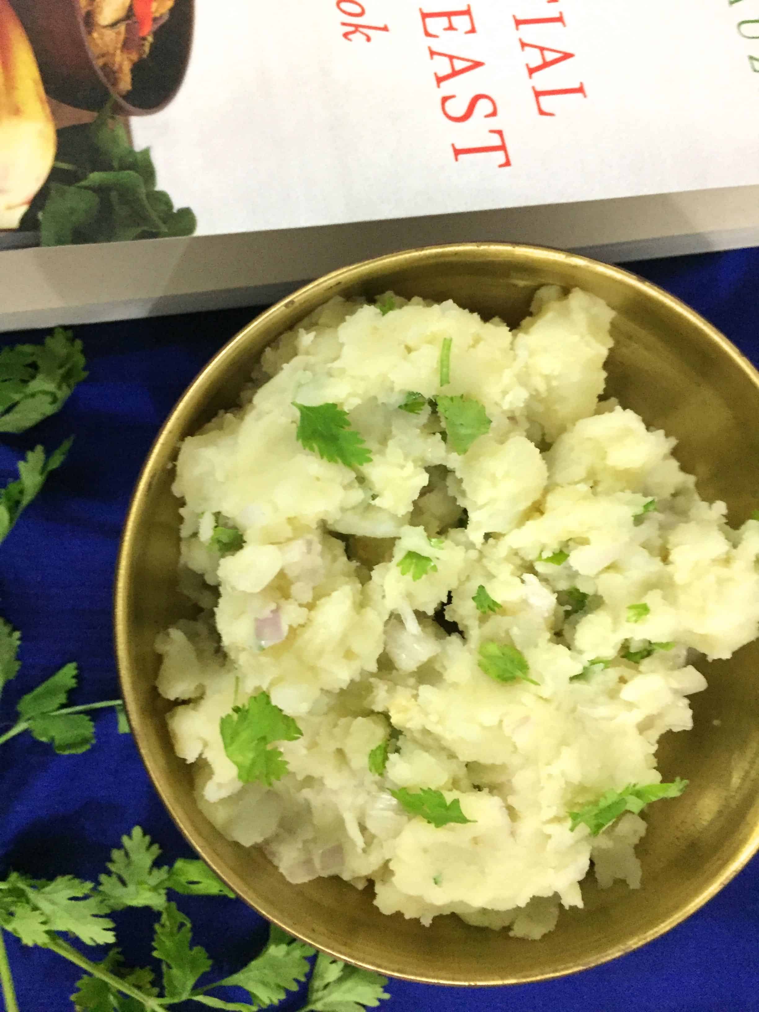 Alu Pitika - mashed potatoes in a bowl with cilantro garnish and a book just visible at the edge