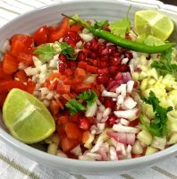 Kachumber Salad A colourful salad of chopped tomatoes, onion, carrot, cucumber and raw mango in a grey bowl garnished with pomegranates and green chilli