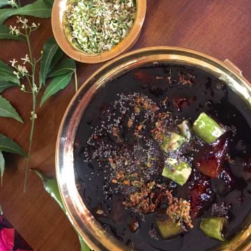 Raw Mango Pachadi for Tamil New Years Day in a brass bowl with a tempering of chilies and mustard seeds and garnish of Neem flowers