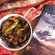 Kashmiri Green Apple Brinjal Curry or Bom Chount Wangan Sabzi of fried eggplant and green apple cooked in spices, in a white bowl with a silk stole and book on the Himalayas alongside