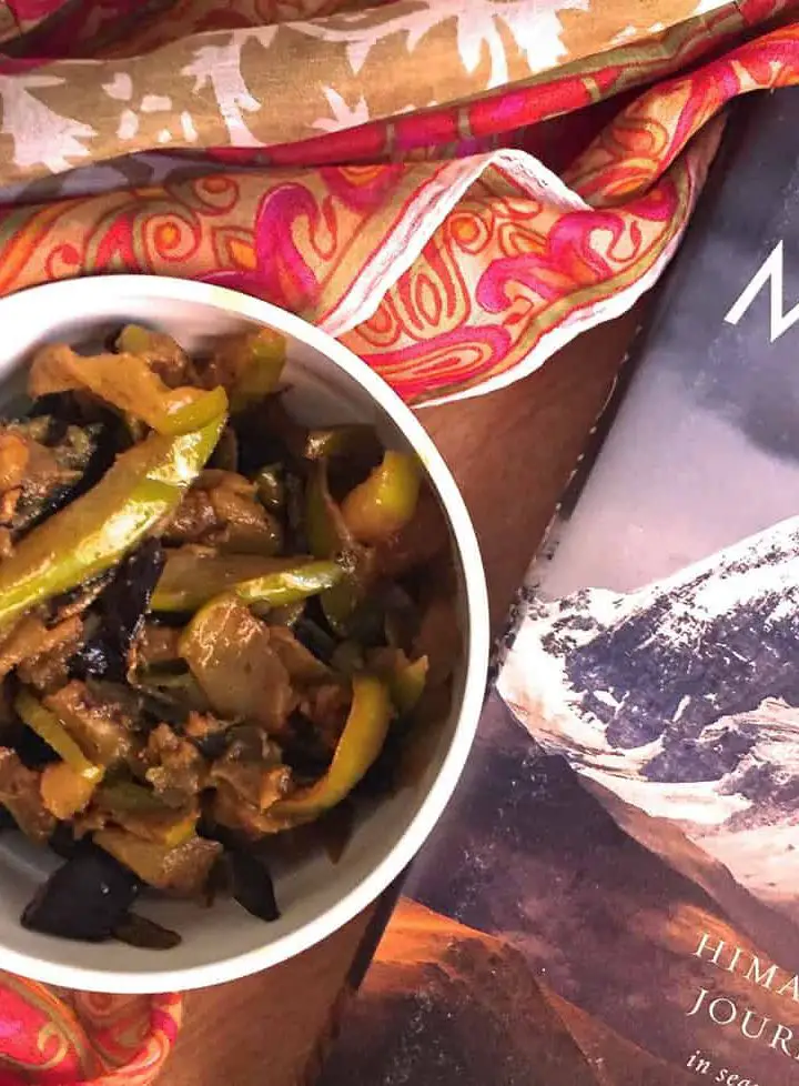 Kashmiri Green Apple Brinjal Curry or Bom Chount Wangan Sabzi of fried eggplant and green apple cooked in spices, in a white bowl with a silk stole and book on the Himalayas alongside