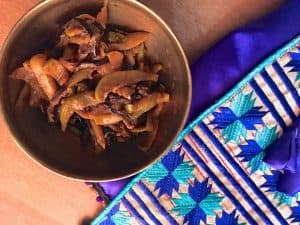 Kashmiri Green Apple Baingan Curry - a brass bowl of brinjal and apples cooked in spices, with a purple and blue silk jacket alongside