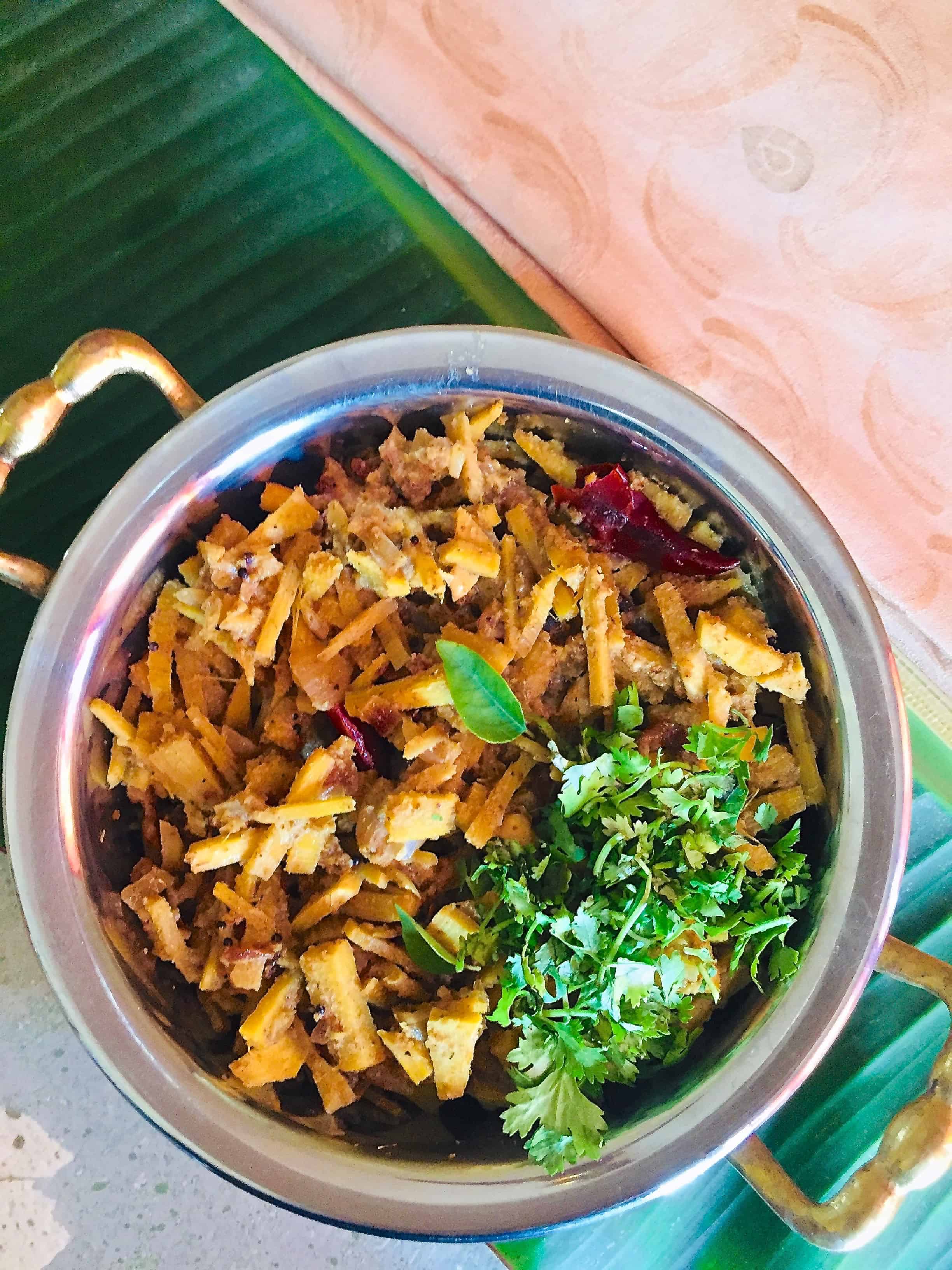 Bamboo shoot curry served in a brass bowl with garnish of coriander leaves, resting on a banana leaf with a pale pink mysore silk saree alongside