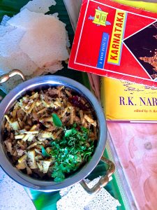 A bowl of bamboo shoot curry with a garnish of coriander leaves and with props showing the Karnataka theme- A guide book to Karnataka, a book by R K Narayanan who lived at Mysore, a Mysore silk saree