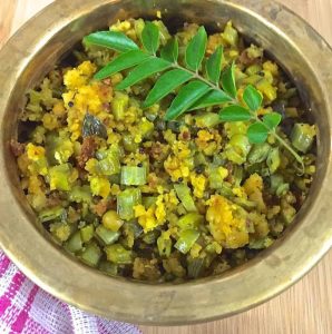 A brass bowl with Kothavarangai Paruppu Usili or Cluster beans in Lentil Paste curry, with a sprig of curry leaves on top and a white and pink striped napkin on the left