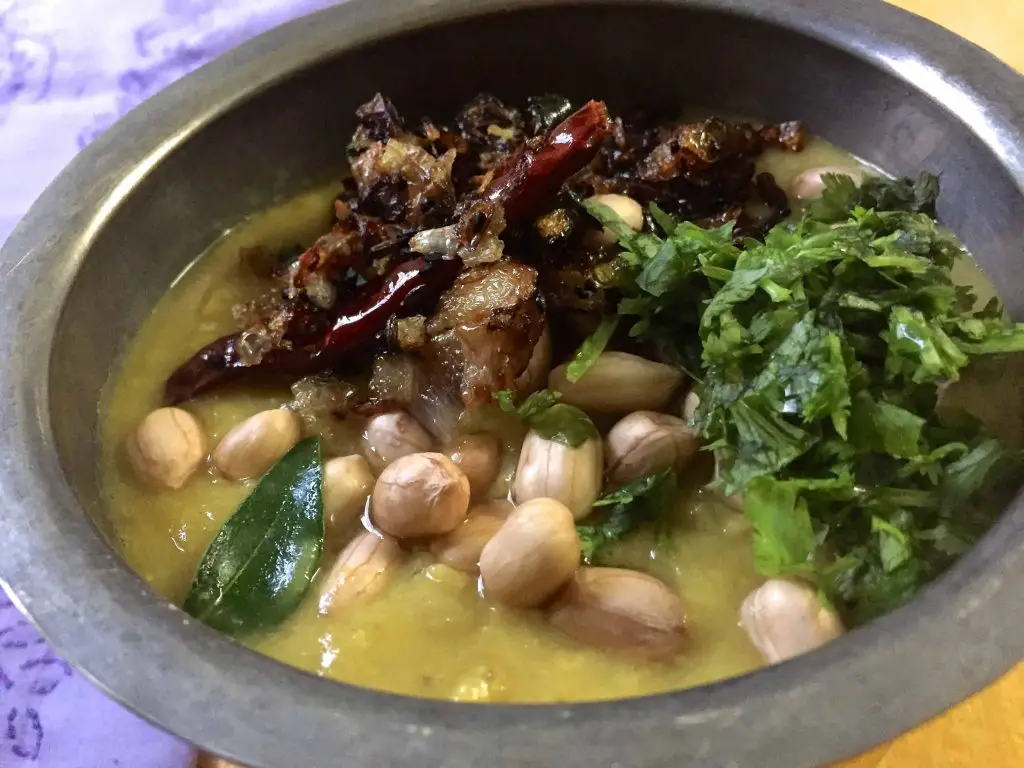 A bowl of yellow lentils garnsihed with peanuts, red chili, fried onion, curry leaves