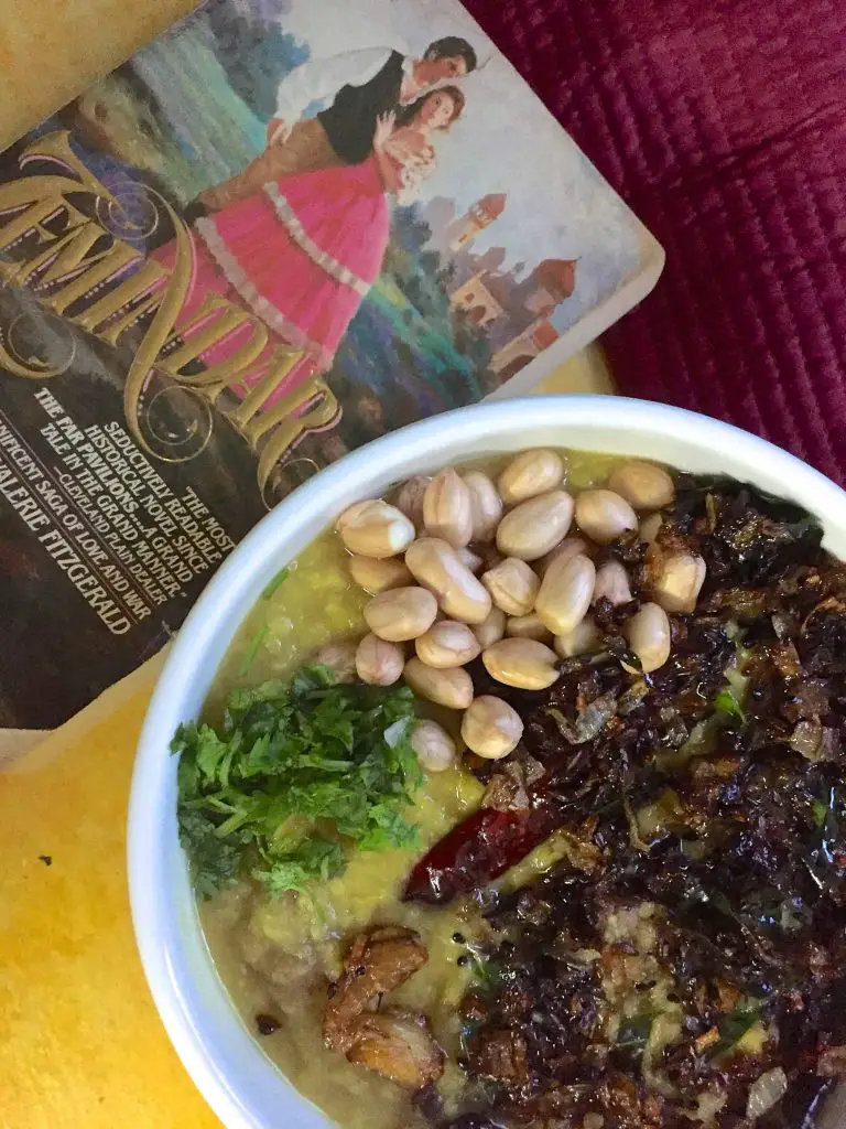 A white bowl with Arhar ki khatti Dal in the Lucknow style, garnished with peanuts and tempered with onions and garlic, and a novel based in Lucknow alongside