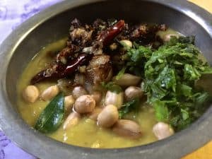 A bowl of Arhar ki khatti Dal garnished with raw peanuts soaked in water and tempered with onion and garlic