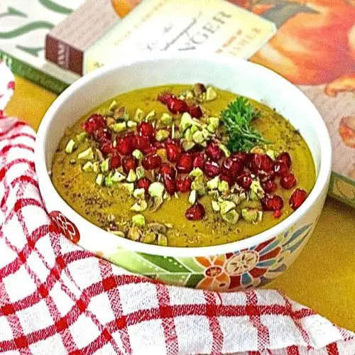 Curried Roasted Pumpkin Soup with apples and Indian spices including turmeric, in a white bowl and a garnish of ruby red pomegranate arils and crushed pista nuts