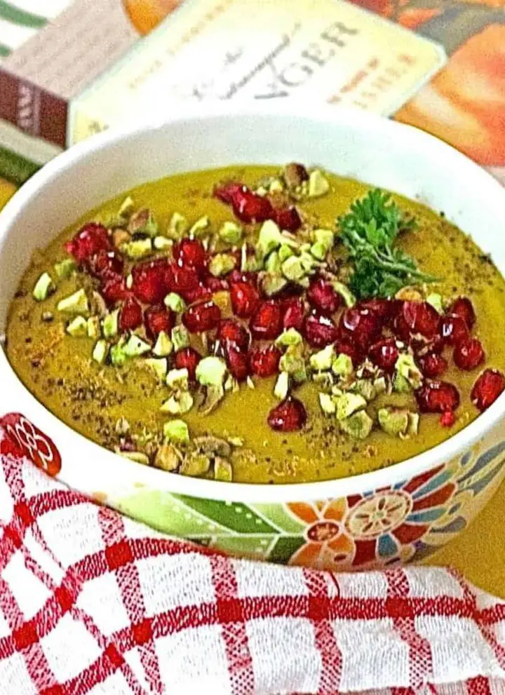 Curried Roasted Pumpkin Soup with apples and Indian spices including turmeric, in a white bowl and a garnish of ruby red pomegranate arils and crushed pista nuts