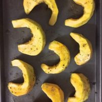 Peeled pumpkin sliced into crescents and drizzled with olive oil, pepper salt and rosemary, ready for baking