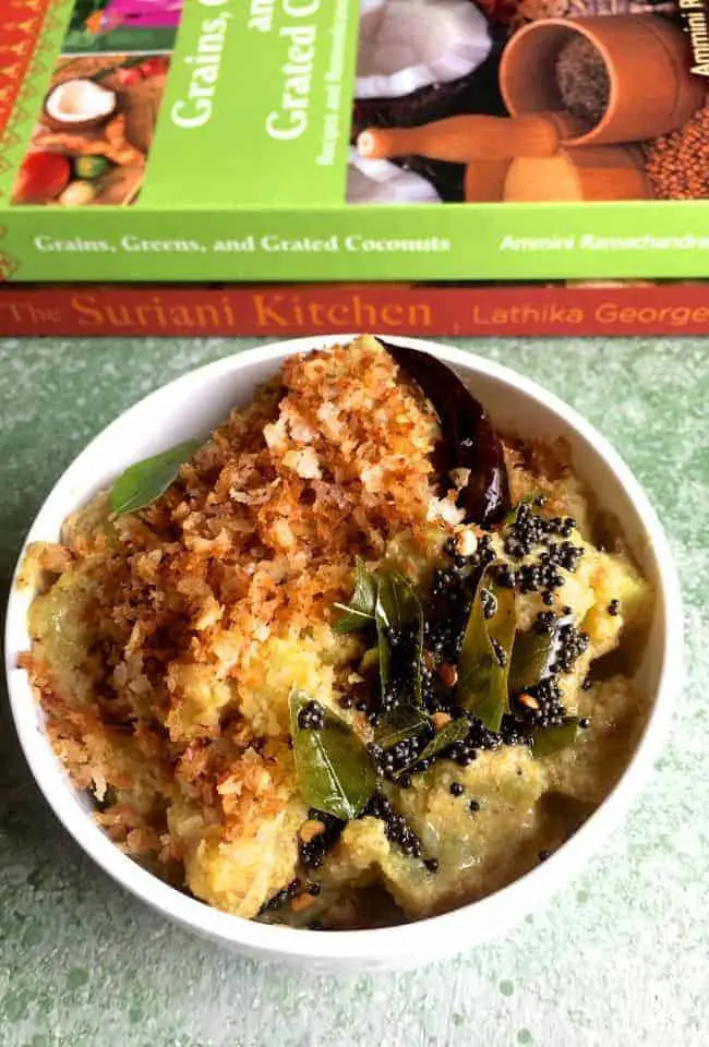 Raw banana dry curry with roasted coconut in a white edged bowl. Two Keral cuisine cook books in green and orange, in the background