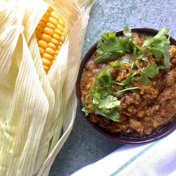 Makai ki sabzi, a spicy corn curry. Served in a bowl garnished with coriander leaves and with a corn cob on the side