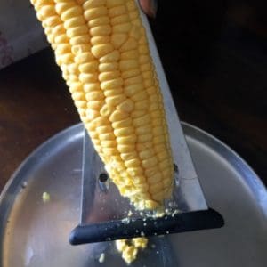 Fresh corn on the cob being grated with a box grater