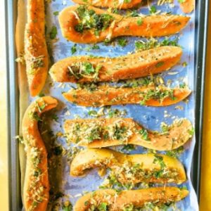 Butternut squash slices dipped in herbs and parmesan arranged on a baking tray ready to bake
