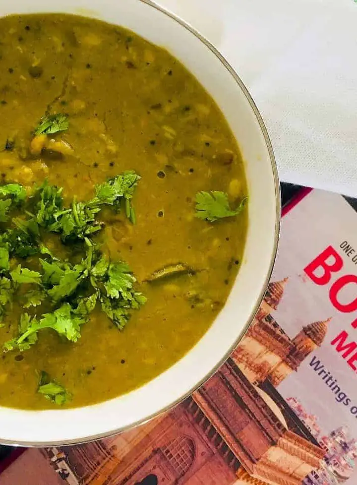 Comfort food Maharashtrian Amti Dal with Goda Masala in a large bowl with coriander leaves garnish and a book on Mumbai alongside