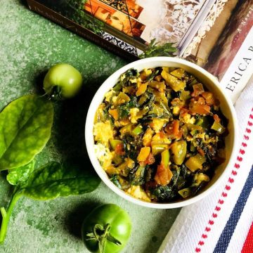 A bowl of greens - saag of radish greens spinach curry with green tomatoes and a white red black napkin and a book on food on a green background