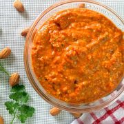 Spanish Romesco Sauce from charred red peppers almonds and tomatoes in a bowl resting on a red striped napkin to one side and with almonds and parsley scattered on the left