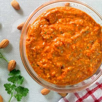 Spanish Romesco Sauce from charred red peppers almonds and tomatoes in a bowl resting on a red striped napkin to one side and with almonds and parsley scattered on the left