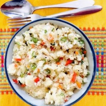 Hot tasty breakfast Vegetable rava Upma with semolina flour. A bowl of Upma on a yellow patterned runner with a steel fork and spoon above