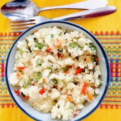 Hot tasty breakfast Vegetable rava Upma with semolina flour. A bowl of Upma on a yellow patterned runner with a steel fork and spoon above