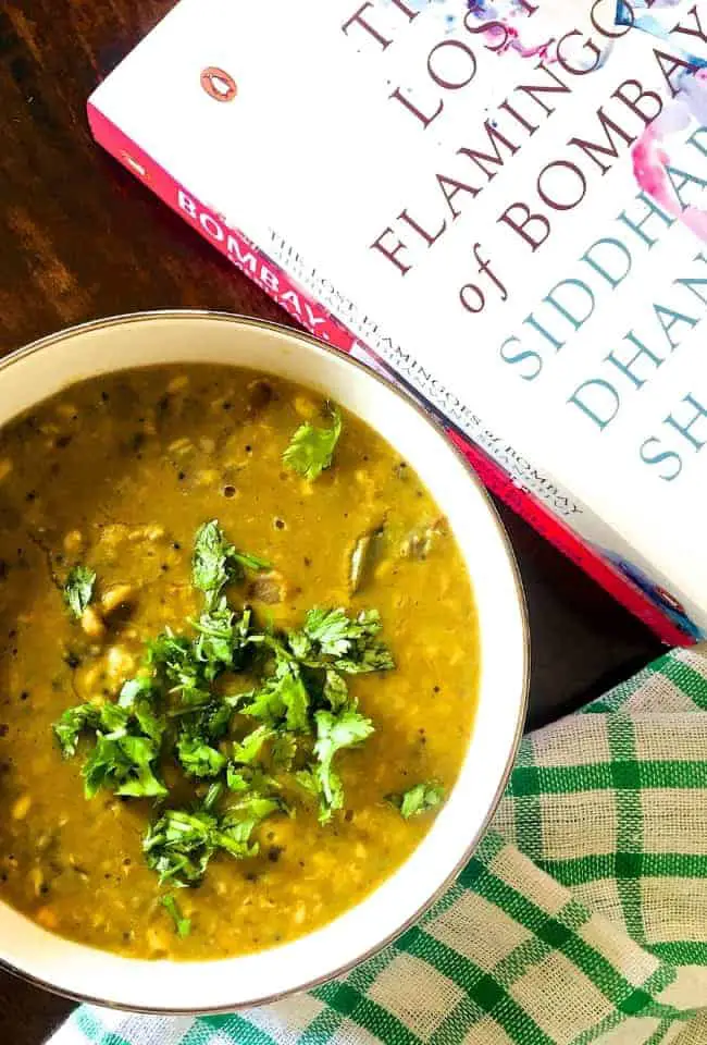 A bowl of Amti Dal with Goda Masala,with a checked green napkin below and a book on Bombay alongside