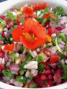 Sliced seasonal vegetables garnished with an orange edible flower with a citrusy dressing