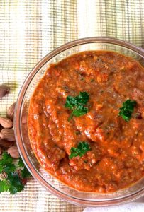A large bowl of Romesco Sauce from Red peppers and almonds, tomato, garnished with parsley and with almonds and parsley by the side