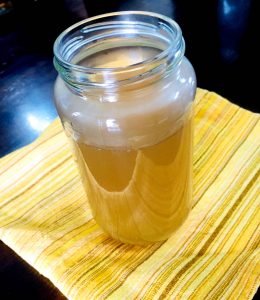 A jar of homemade stock on a yellow background