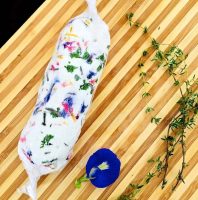 Party time deserves this Edible flower and herb butter. Here is it is rolled and wrapped like a sausage and kepto on a striped wooden board with a blue flower and some thyme sprigs alongside