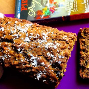 Easy Eggless Christmas Fruit Cake with no added sugar. Set on a purple sheet with a book on Pies on one side and a slice of the cake alongside