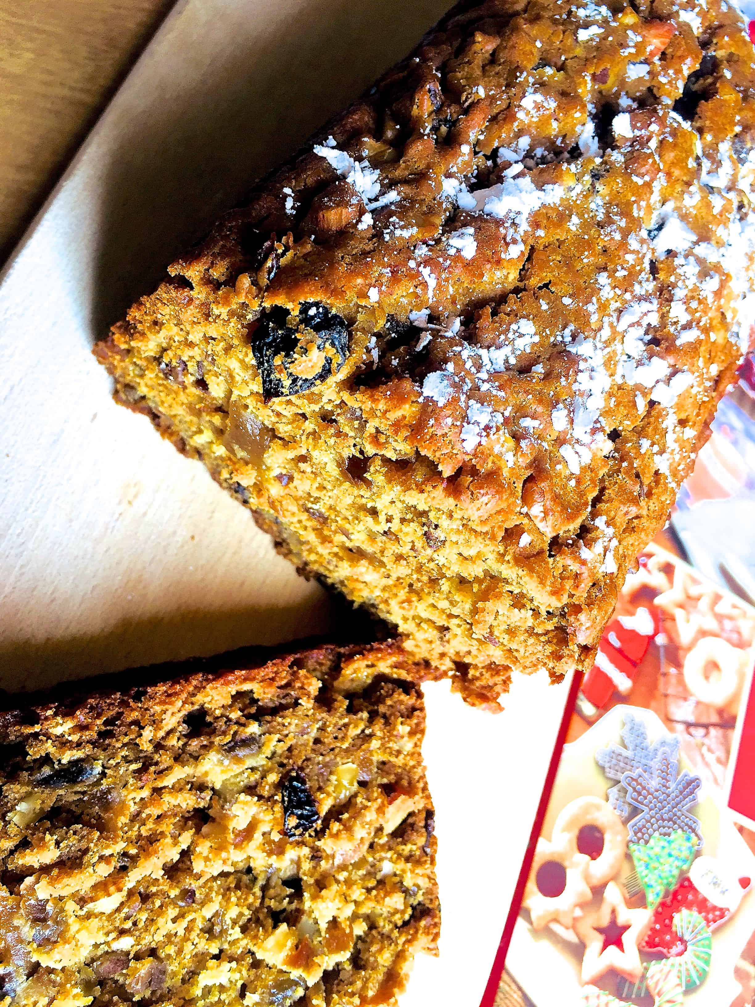Christmas Fruit cake with no eggs and no added sugar, sliced and on a wooden board with a book of Christmas recipes alongside