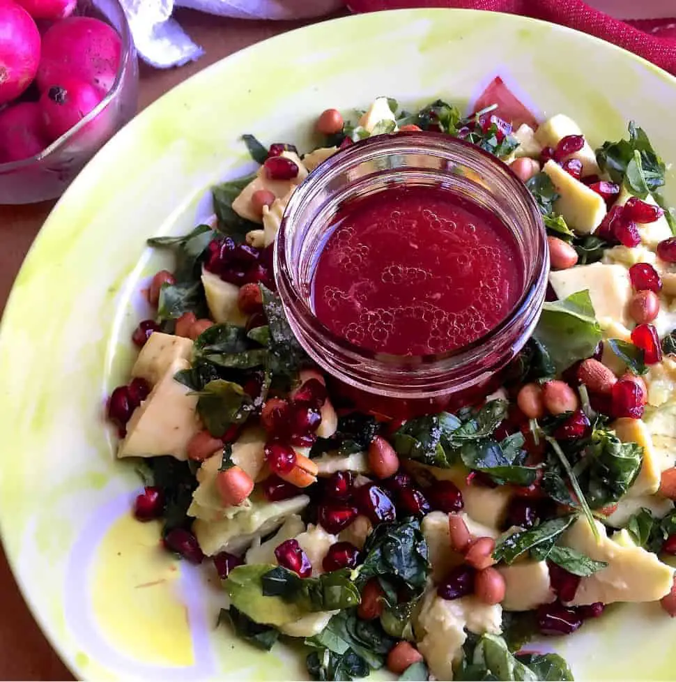 Avocado Fenugreek Leaves Salad with Peanuts, feta and pomegranate arranged on a green plate with pink dressing in the centre and reddish pink radishes in a bowl