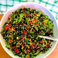 A bowl of finely chopped red tomatoes, green parsley and beige bulgar wheat making up a Levantine Tabbouleh, the parsley bulgar tomato salad, on a green and white checked napkin, on an orange background
