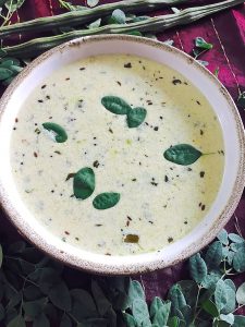 A wide bowl of cream coloured murungai keerai morekuzambu or drumstick leaves in a yogurt coconut stew