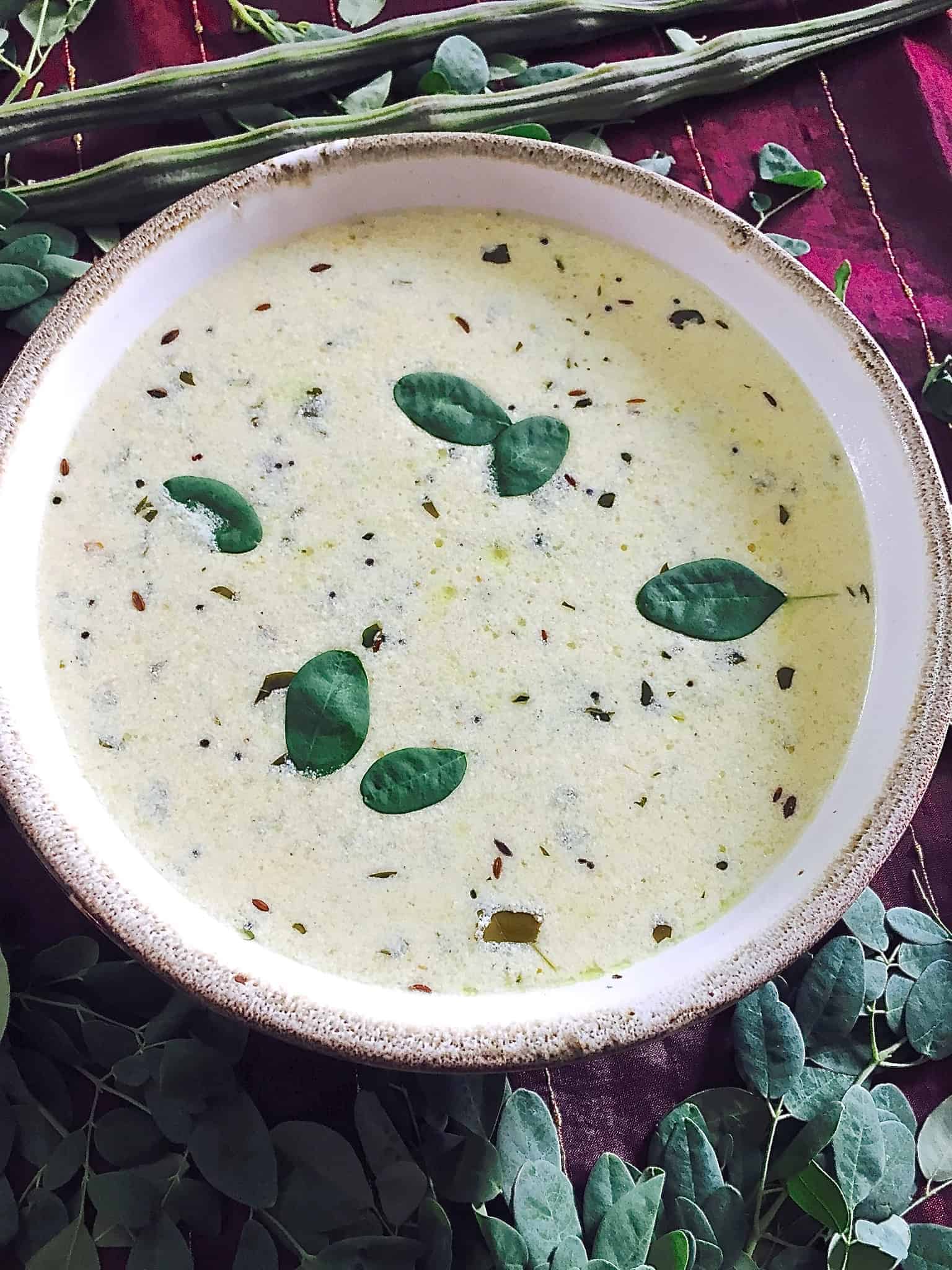 A wide bowl of cream coloured murungai keerai morekuzambu or drumstick leaves in a yogurt coconut stew