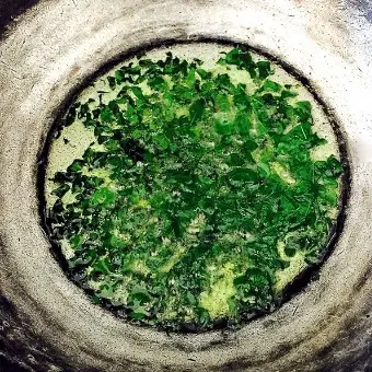 Drumstick leaves or moringa leaves being sauteed in a pan of coconut oil