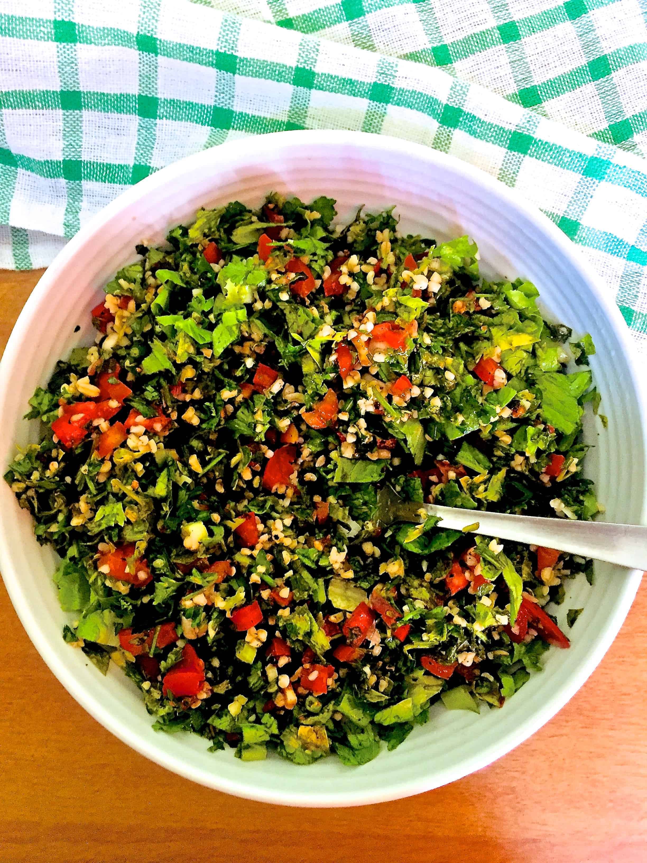 Red and green colourful Levantine Tabbouleh in a white bowl with a green and white checked napkin on an orange background. Finely chopped Green flat leaf parsely, red tomatoes, white creamy bulgar, green romaine lettuce