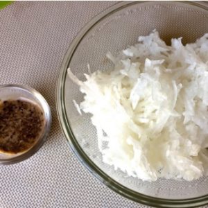 Grated white radish in a glass bowl with a smaller glass bowl of black sesame paste, all on a dull white background