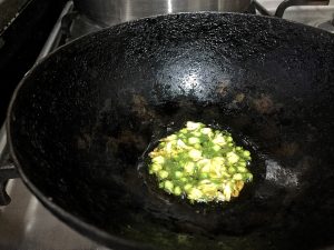 A black iron kadai/ frying pan, with white and green moringa flowers being fried in ghee or clarified butter, to garnish the drumstick corn carrot soup