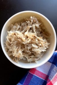 White bowl of radish salad - grated white radish mixed with brown paste of black sesame, on a blue black background, edge of blue red napkin seen top right