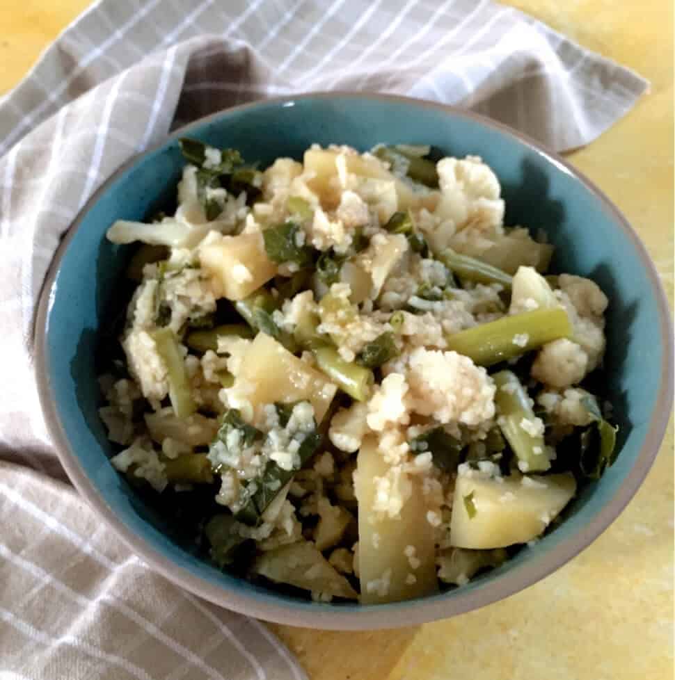 A blue bowl with boiled cauliflower florets, leaves and stalks, Potato and beans for Mizo Bai a vegetable stew from India's NE Mizoram. A pale brown checked napkin to the left