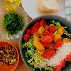 Arugula Pesto Pasta in Cherry Tomato Sauce:A bluish green bowl with fettuccine pasta covered with pesto, topped with a sauce of red and yellow cherry tomatoes and parmesan